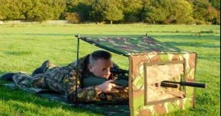 Man aiming an air rifle through a small camouflage hide